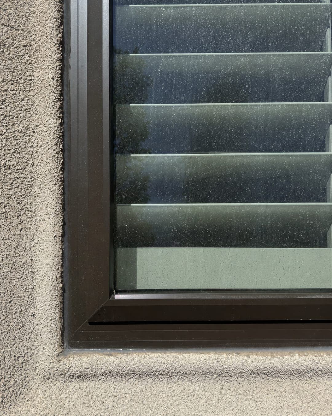 Window glass covered in dried hard-water spots from sprinkler overspray, before treatment