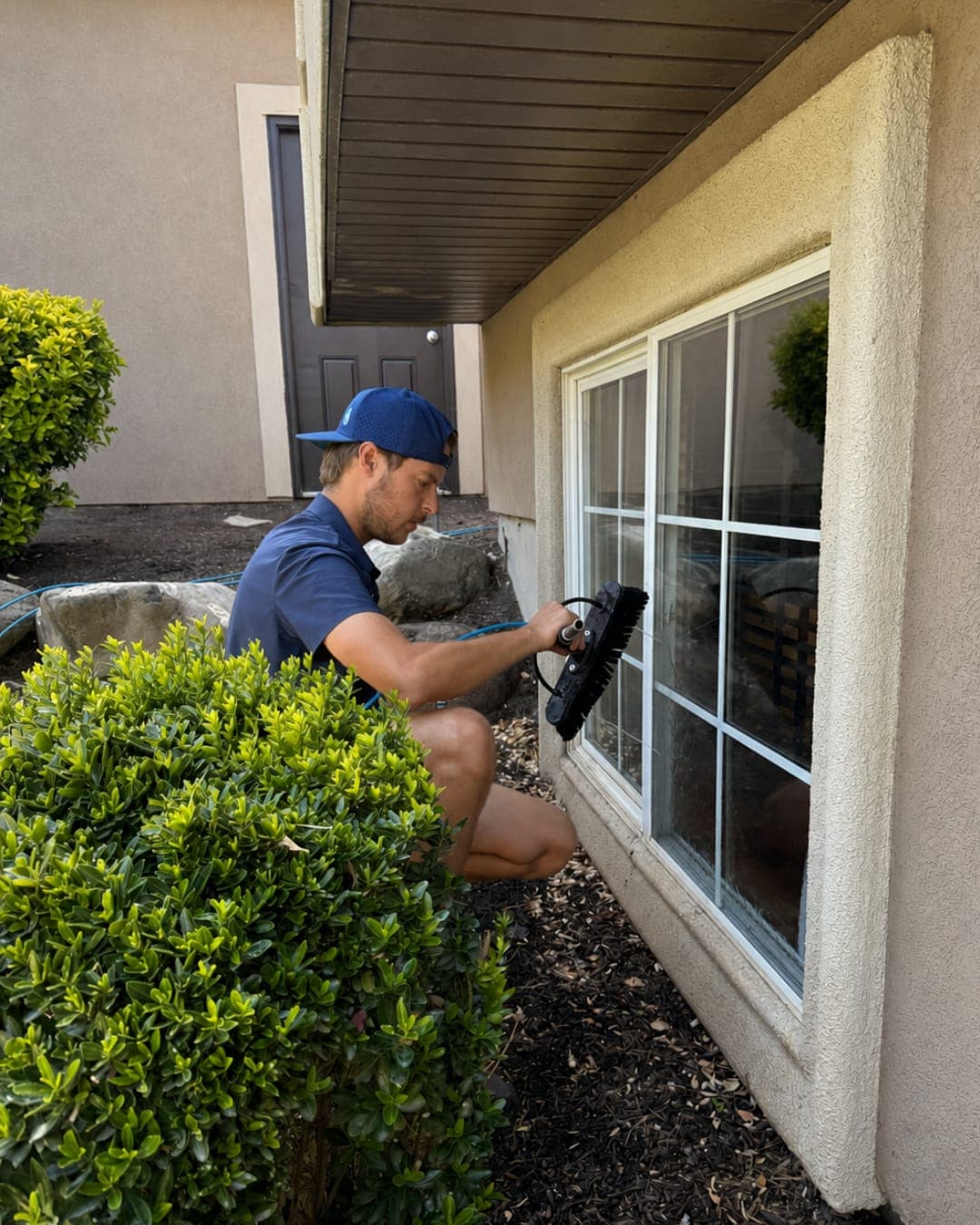 Glide technician cleaning a lower window near landscaping, where hard water and sprinkler spotting shows up first